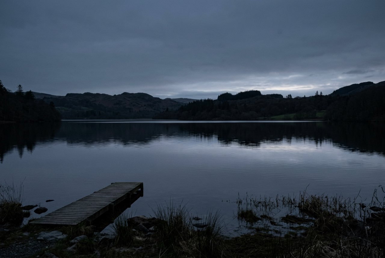 Half past four in the morning: a still lake with the far shore just becoming visible, no wind, everything grey blue