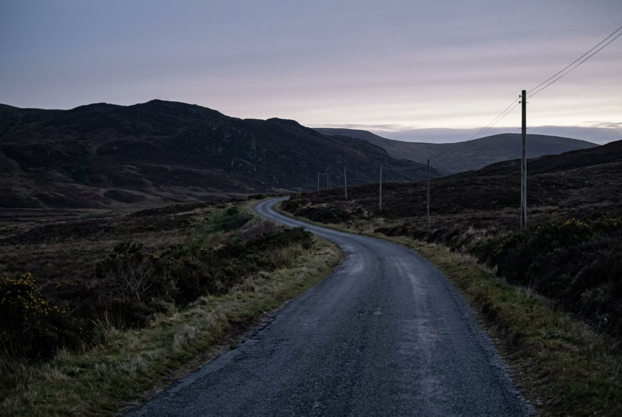 Four in the morning: an empty upland road under a sky just beginning to grey, the hills still black shapes