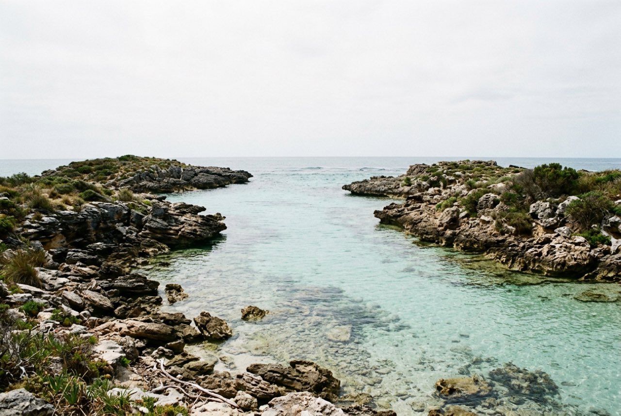 Eleven in the morning: a clear shallow channel between two low rocky islands, hard bright overcast, water very clear
